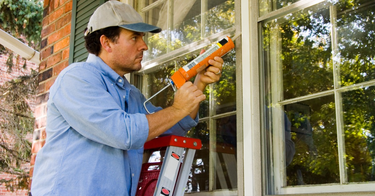A man applying caulk around a window frame to seal gaps and improve insulation, helping prevent drafts and energy loss.