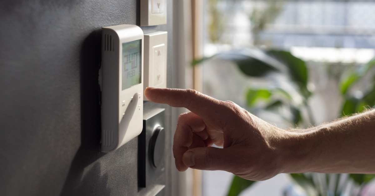 A person adjusts the settings on a wall-mounted digital thermostat that displays indoor temperature controls.