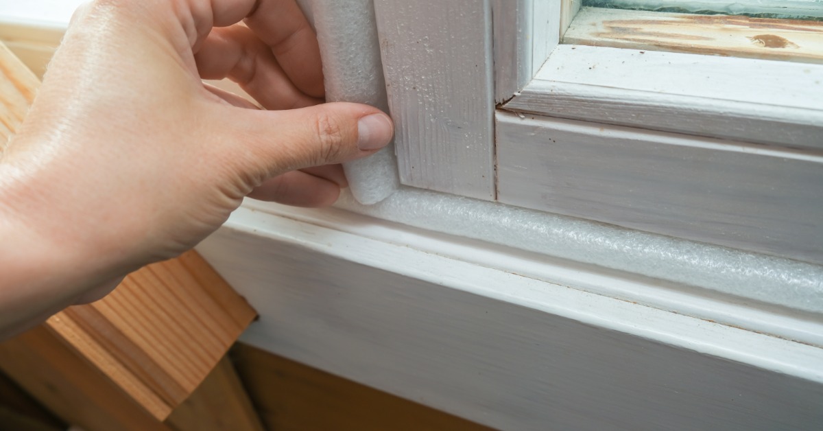 A close-up of a person applying insulation material around a window frame to seal the gaps along the edges.