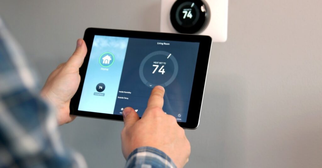 A person uses a tablet with a smart home temperature screen, matching the settings to the thermostat on the wall.